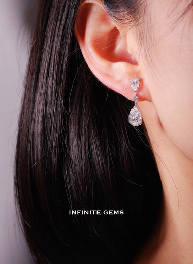 Pear shape lab grown diamond drop earring in 18K white gold, a 0.5ct pear at the lobe linked by a round brilliant to a 1.5ct pear drop, worn on the ear
